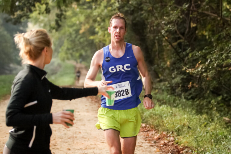 a female race volunteer handing water to a male GRC runner